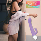 A woman in a white shirt leans against a railing outdoors, with the VeDO Wink Rabbit Vibe - Lavender prominently displayed in the foreground. The text "VeDO let your body vibe" appears in the upper right corner, emphasizing its design that targets both the G-Spot and Clitoris.